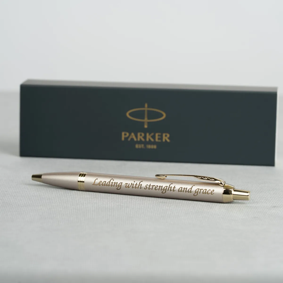 Długopis Parker IM Professionals Monochrome Champagne z grawerem „Leading with strenght and grace” na tle eleganckiego pudełka Parker.