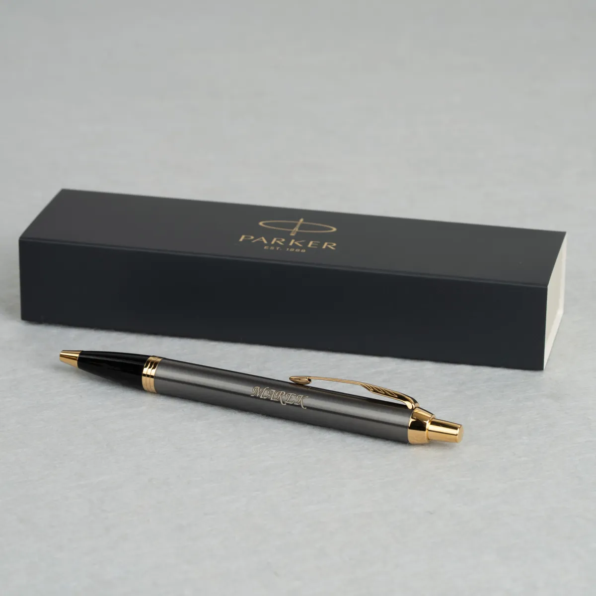 Długopis Parker IM Grey GT z personalizowanym grawerem &bdquo;MAREK&rdquo;, prezentowany na tle eleganckiego firmowego etui Parker