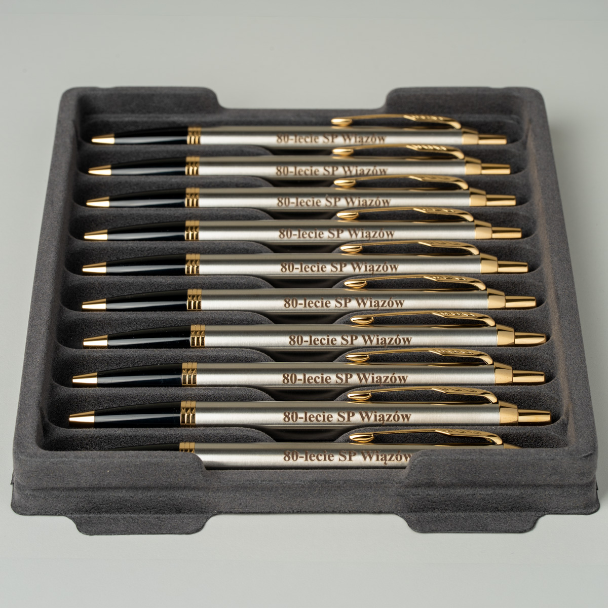Długopisy Parker IM Brushed Metal GT [1931670] z grawerem &bdquo;80-lecie SP Wiąz&oacute;w&rdquo;, ułożone w szarej, piankowej tacy.